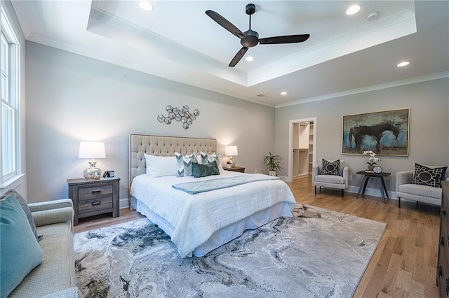 bedroom with baseboards, wood finished floors, a raised ceiling, and recessed lighting