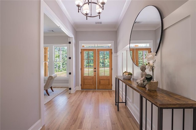 entrance foyer featuring ornamental molding, light wood-type flooring, visible vents, and a notable chandelier