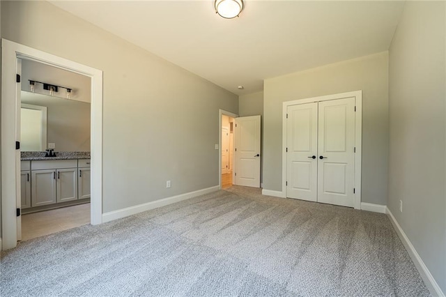 unfurnished bedroom with ensuite bathroom, light colored carpet, a sink, baseboards, and a closet