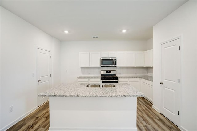 kitchen featuring light stone counters, stainless steel appliances, a center island with sink, and white cabinets