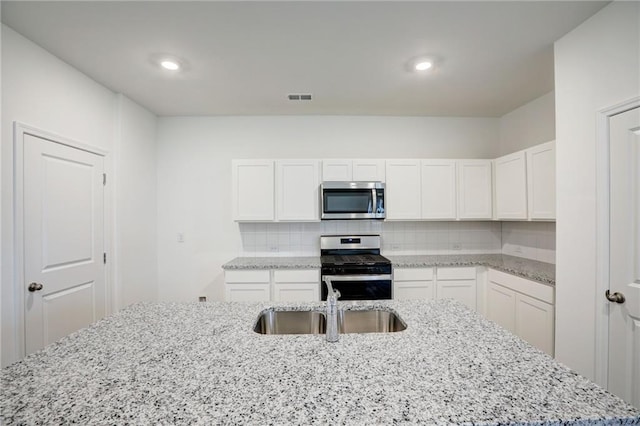 kitchen with light stone counters, decorative backsplash, stainless steel appliances, and white cabinets