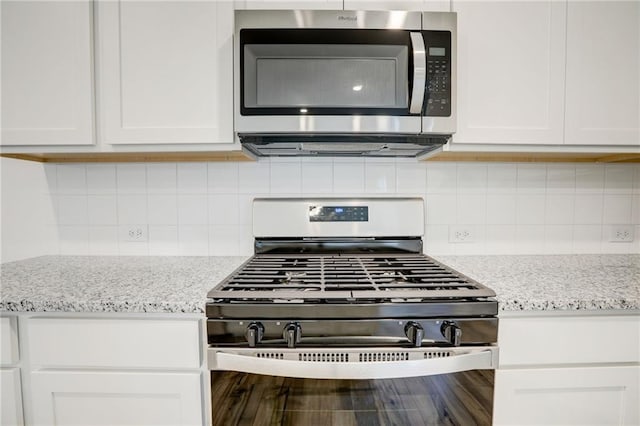 kitchen featuring stainless steel appliances, white cabinetry, light stone countertops, and decorative backsplash