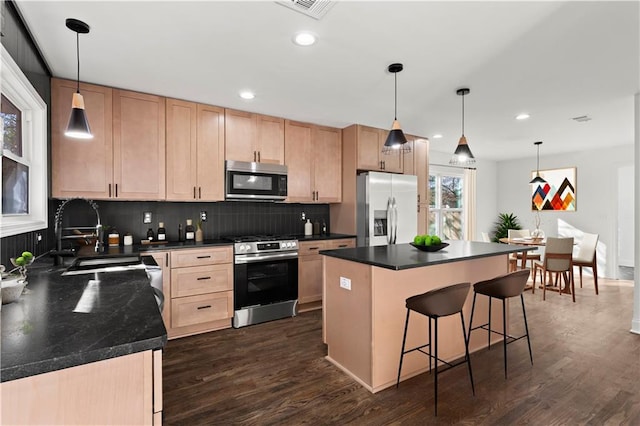 kitchen featuring stainless steel appliances, light brown cabinetry, dark countertops, and dark wood finished floors