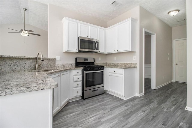 kitchen featuring light stone counters, a sink, white cabinets, light wood-style floors, and appliances with stainless steel finishes