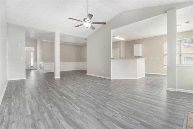 unfurnished living room featuring baseboards, wainscoting, lofted ceiling, ceiling fan, and wood finished floors