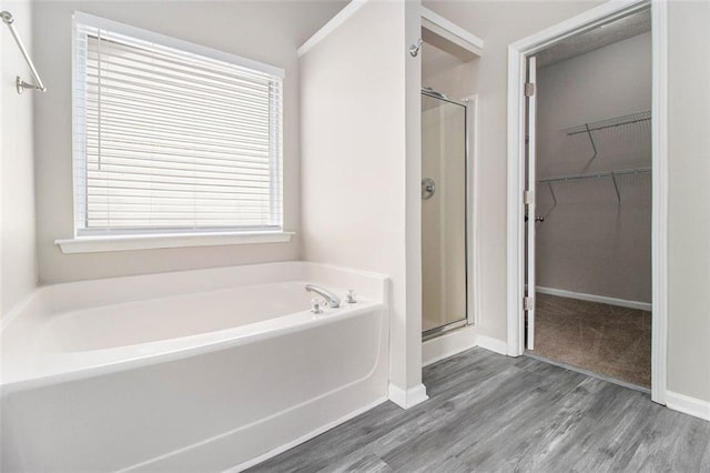 full bathroom featuring a stall shower, a walk in closet, wood finished floors, and a bath