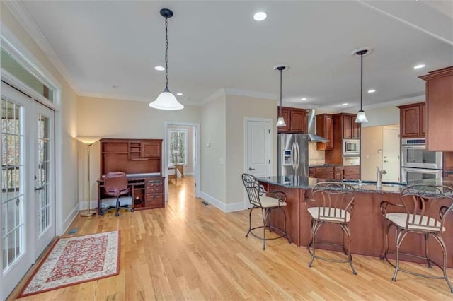 kitchen featuring ornamental molding, french doors, appliances with stainless steel finishes, a kitchen bar, and wall chimney range hood