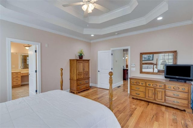 bedroom featuring ensuite bath, a tray ceiling, light wood-style flooring, and crown molding