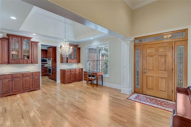 foyer with a tray ceiling, a notable chandelier, ornamental molding, and light wood finished floors