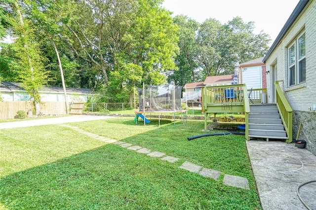 view of yard with stairway, a trampoline, a wooden deck, and fence