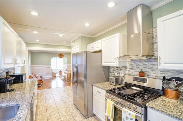 kitchen featuring stainless steel appliances, white cabinets, wainscoting, wall chimney exhaust hood, and crown molding