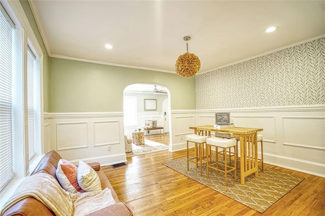 dining area featuring arched walkways, a wainscoted wall, crown molding, recessed lighting, and light wood-style flooring