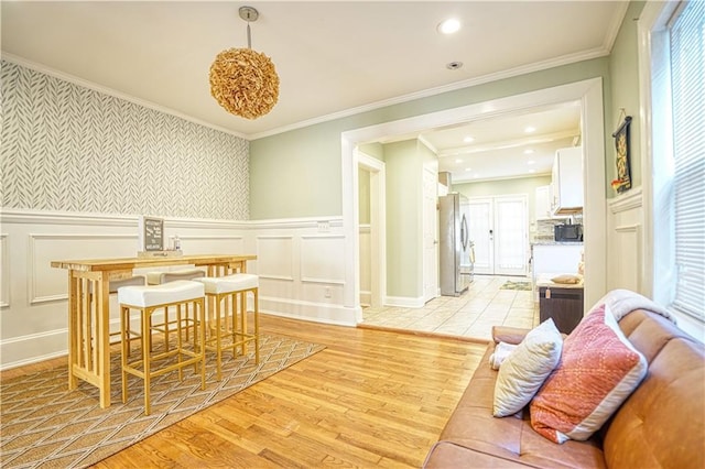 dining area featuring light wood-style floors, recessed lighting, crown molding, and a wainscoted wall