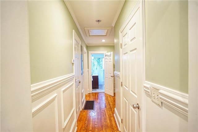 corridor with attic access, a wainscoted wall, wood finished floors, crown molding, and a decorative wall