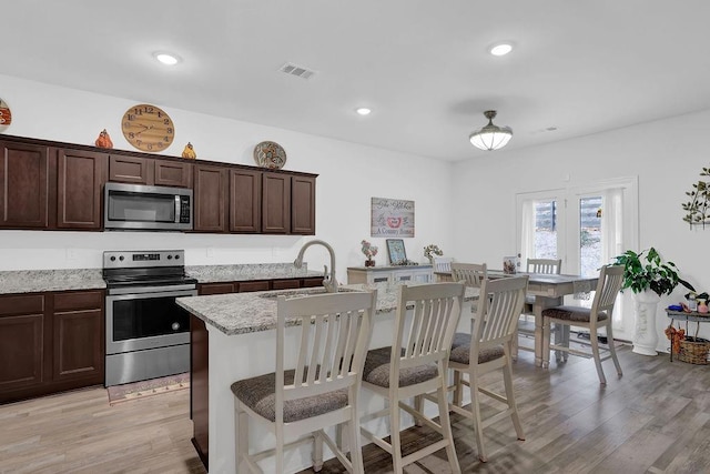 kitchen featuring light stone countertops, an island with sink, light wood-type flooring, appliances with stainless steel finishes, and sink