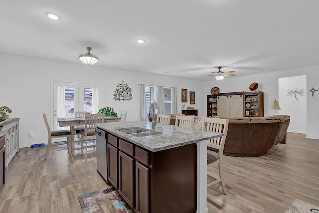 kitchen with sink, dishwasher, light stone counters, dark brown cabinets, and a barn door