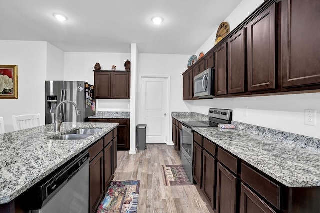 kitchen with light stone countertops, light wood-type flooring, a kitchen island with sink, appliances with stainless steel finishes, and sink