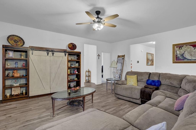 living room with ceiling fan, a barn door, and light hardwood / wood-style floors