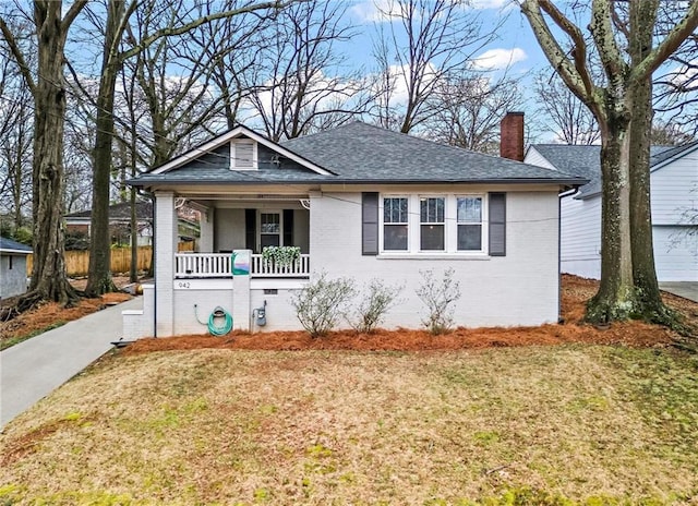 bungalow-style home featuring a porch, a front yard, brick siding, and a chimney