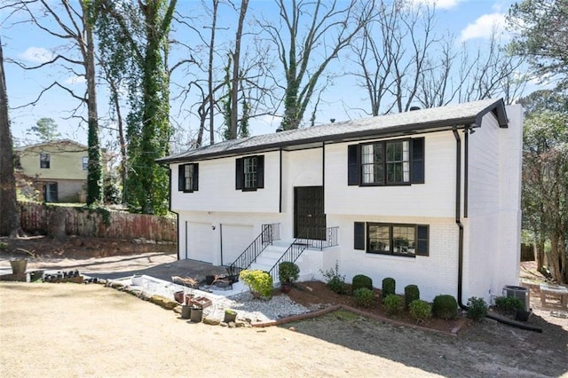 split foyer home featuring driveway, an attached garage, fence, central AC, and brick siding