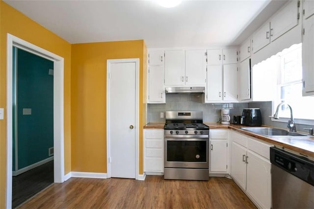 kitchen with decorative backsplash, white cabinets, appliances with stainless steel finishes, under cabinet range hood, and a sink