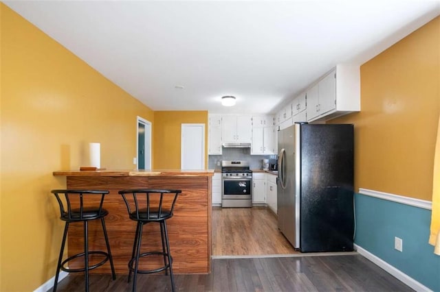 kitchen with white cabinets, a breakfast bar area, a peninsula, stainless steel appliances, and under cabinet range hood