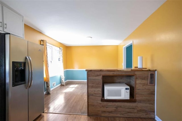 kitchen featuring baseboards, white cabinets, white microwave, wood finished floors, and stainless steel refrigerator with ice dispenser