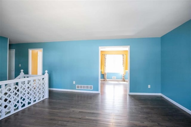 spare room featuring dark wood-style floors, visible vents, and baseboards