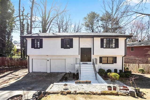 raised ranch with a garage, brick siding, fence, and driveway