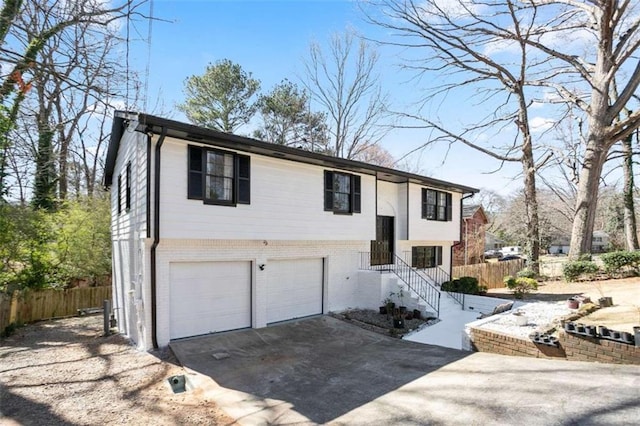 raised ranch with brick siding, driveway, an attached garage, and fence