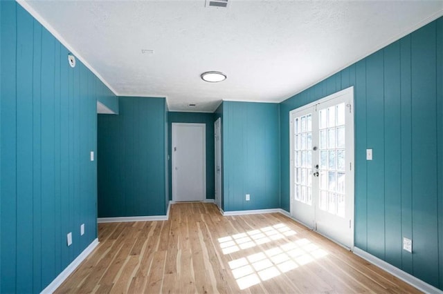 spare room featuring crown molding, baseboards, wood finished floors, and french doors