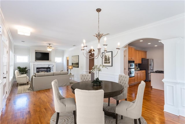 dining room with ornate columns, crown molding, ceiling fan with notable chandelier, and light hardwood / wood-style flooring