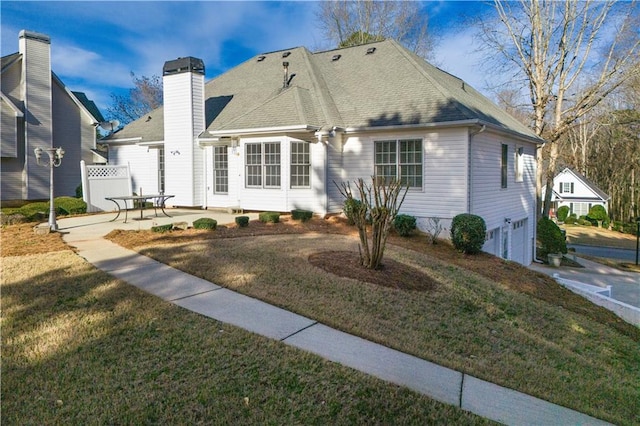exterior space with a chimney, roof with shingles, an attached garage, a patio area, and a front yard