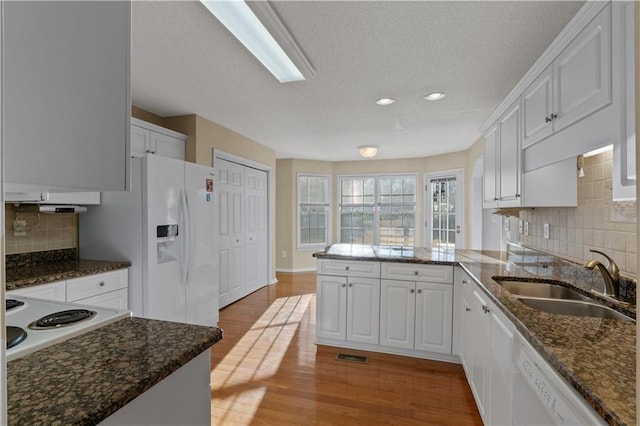 kitchen with a peninsula, white appliances, a sink, white cabinets, and light wood finished floors