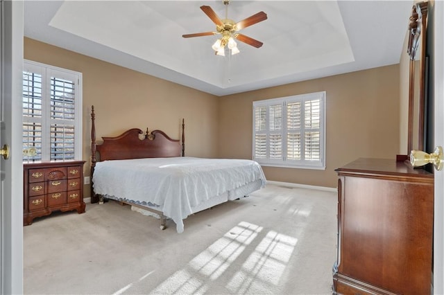 bedroom with ceiling fan, baseboards, a raised ceiling, and light colored carpet
