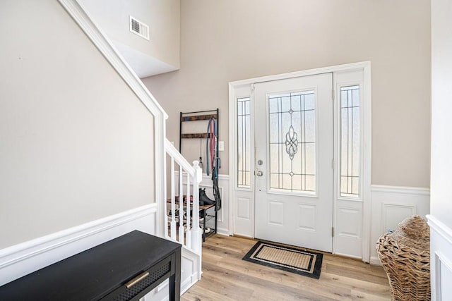 foyer featuring a wainscoted wall, light wood-style flooring, stairs, and visible vents