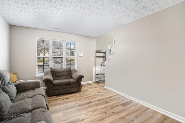 living area featuring a textured ceiling, light wood-style floors, visible vents, and baseboards