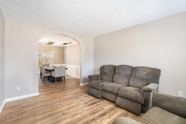 living room featuring visible vents, a wainscoted wall, light wood-type flooring, arched walkways, and a textured ceiling