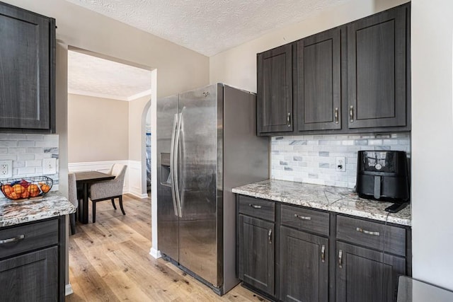 kitchen with light wood-style flooring, stainless steel refrigerator with ice dispenser, a textured ceiling, arched walkways, and decorative backsplash