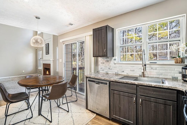 kitchen with tasteful backsplash, dark brown cabinets, dishwasher, a fireplace, and a sink