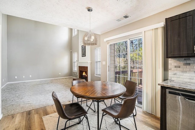 dining space with visible vents, a brick fireplace, baseboards, light wood-style flooring, and a textured ceiling