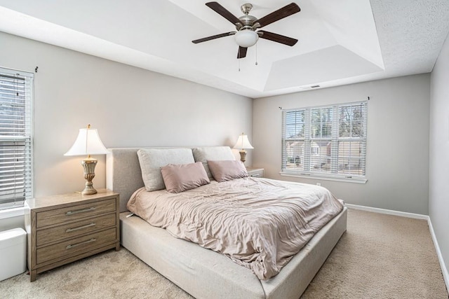 bedroom with a raised ceiling, multiple windows, baseboards, and light carpet