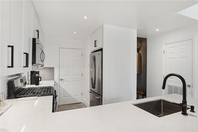 kitchen featuring sink, appliances with stainless steel finishes, white cabinetry, light stone counters, and tasteful backsplash