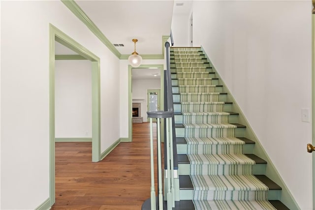 staircase with visible vents, ornamental molding, wood finished floors, a stone fireplace, and baseboards