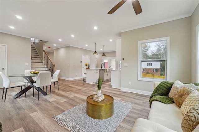 living room with baseboards, stairway, light wood finished floors, and ceiling fan