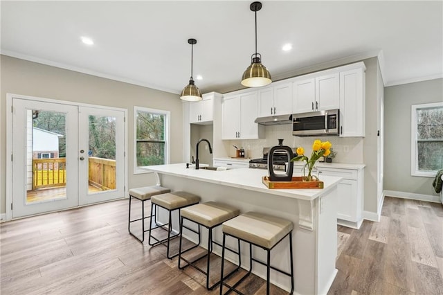 kitchen featuring stainless steel microwave, ornamental molding, under cabinet range hood, plenty of natural light, and range with gas stovetop