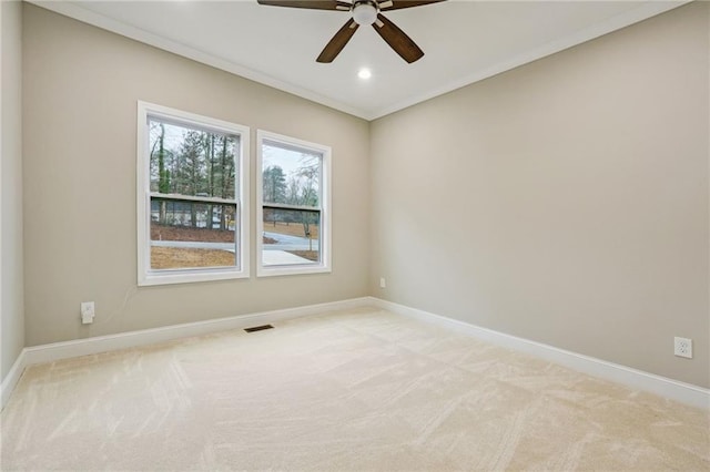 spare room with light colored carpet, ornamental molding, visible vents, ceiling fan, and baseboards