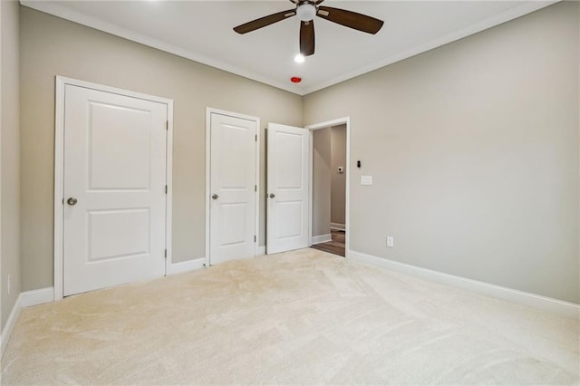 unfurnished bedroom with carpet, baseboards, multiple closets, and ceiling fan