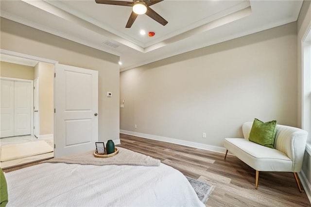 bedroom with wood finished floors, ornamental molding, visible vents, a tray ceiling, and baseboards