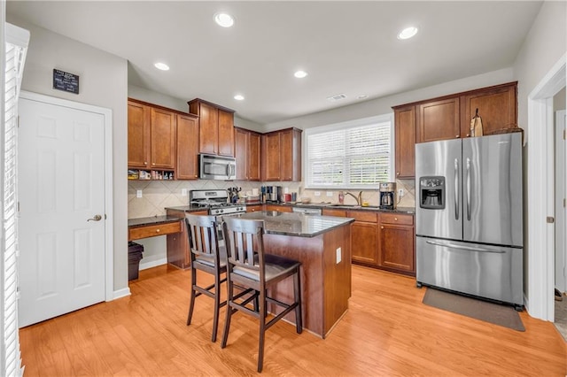 2677 Sardis Chase Ct, Buford, GA 30519 - kitchen featuring appliances with stainless steel finishes, light wood finished floors, brown cabinetry, a breakfast bar area, and decorative backsplash